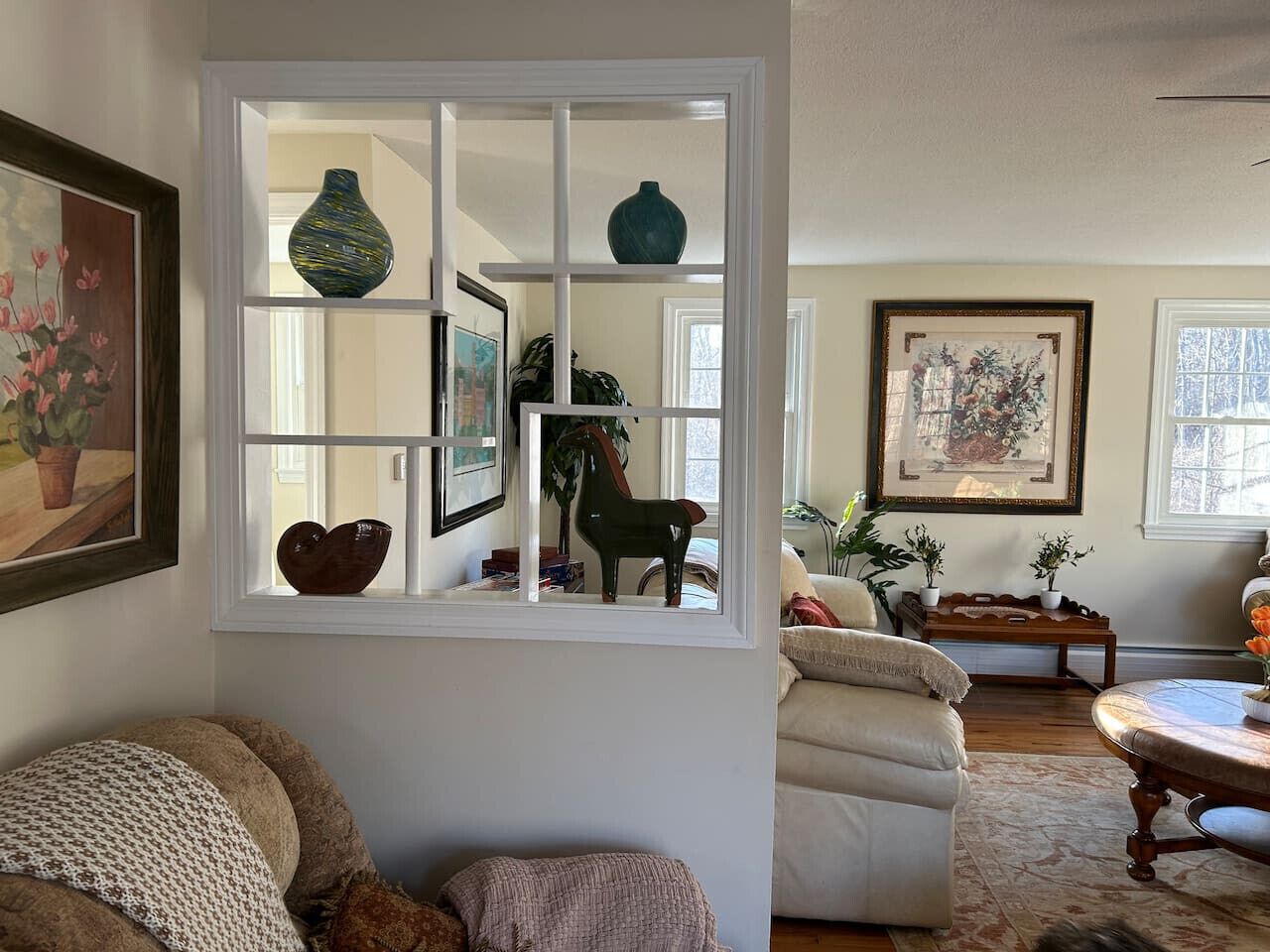 A cozy living room with a white-framed window, a green vase, and a framed painting on the wall.