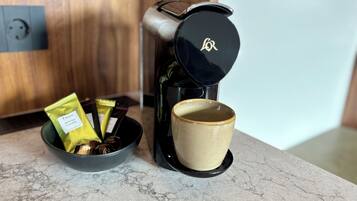 A coffee maker with a cup and a bowl containing coffee pods and a spoon on a marble countertop.