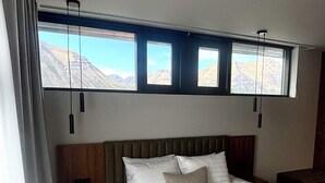 A bedroom with a large bed, a wooden headboard, and a view of mountains through three windows. - Hvanndalir Lodge (Olafsfjordur)