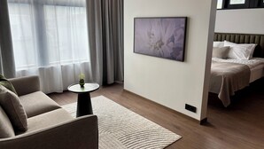 A modern hotel room with a sofa, a small table with a vase, a large abstract painting, and a bed with a headboard. - Hvanndalir Lodge (Olafsfjordur)