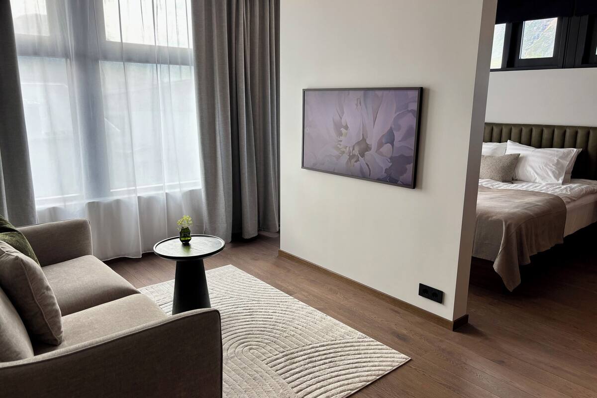 Una habitación de hotel moderna con un sofá, una mesita con un jarrón, un cuadro abstracto grande y una cama con cabecera.