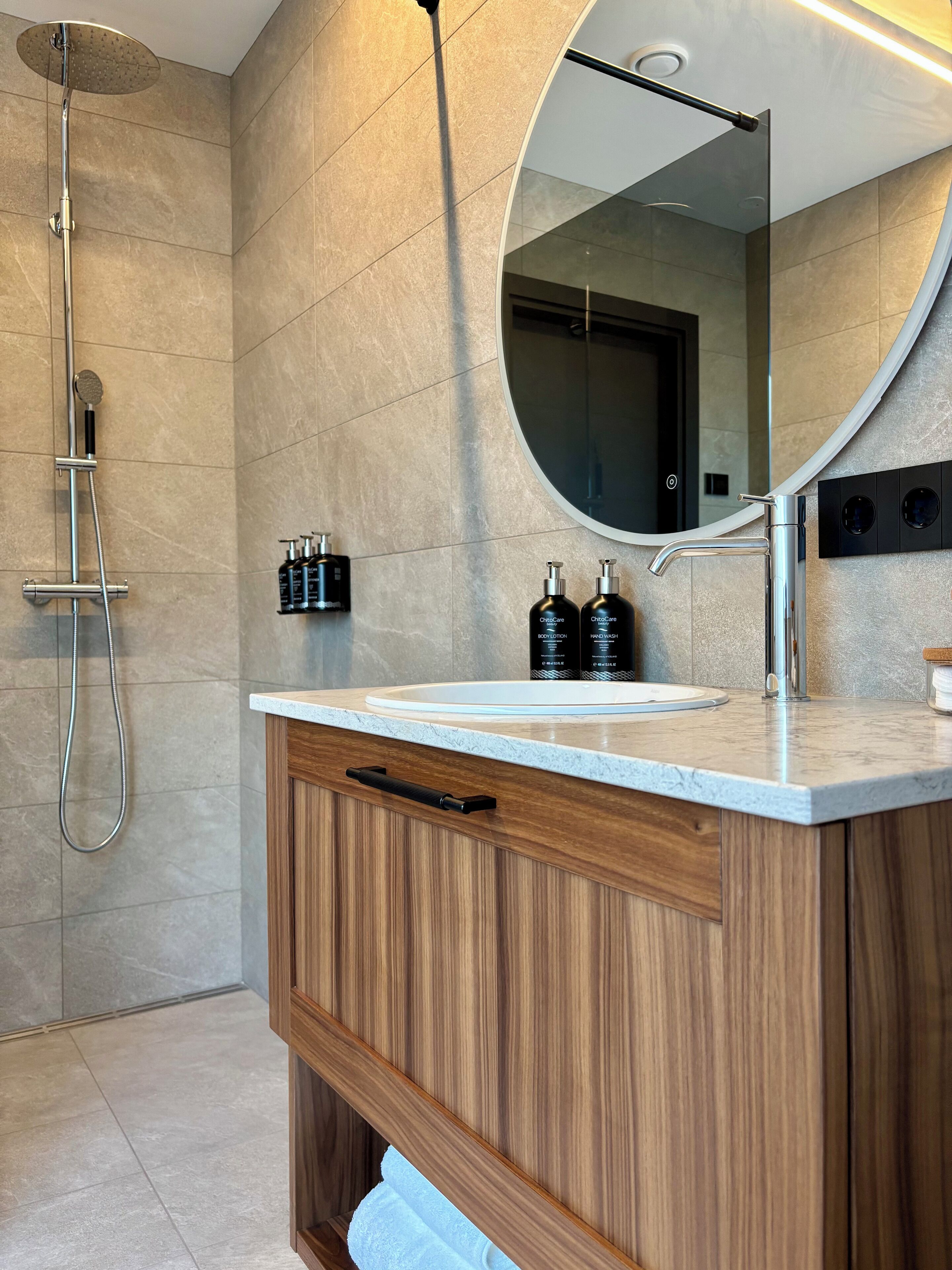Ein modernes Badezimmer mit Waschtisch aus Holz, einem großen Spiegel und einer Dusche.