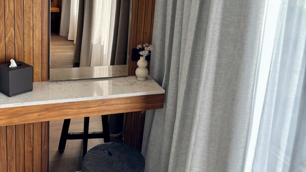 A modern room with a wooden desk, a mirror, a stool, and grey curtains. - Hvanndalir Lodge (Olafsfjordur)
