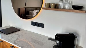 A modern kitchen with a marble countertop, a coffee maker, and a mirror with a circular frame. - Hvanndalir Lodge (Olafsfjordur)