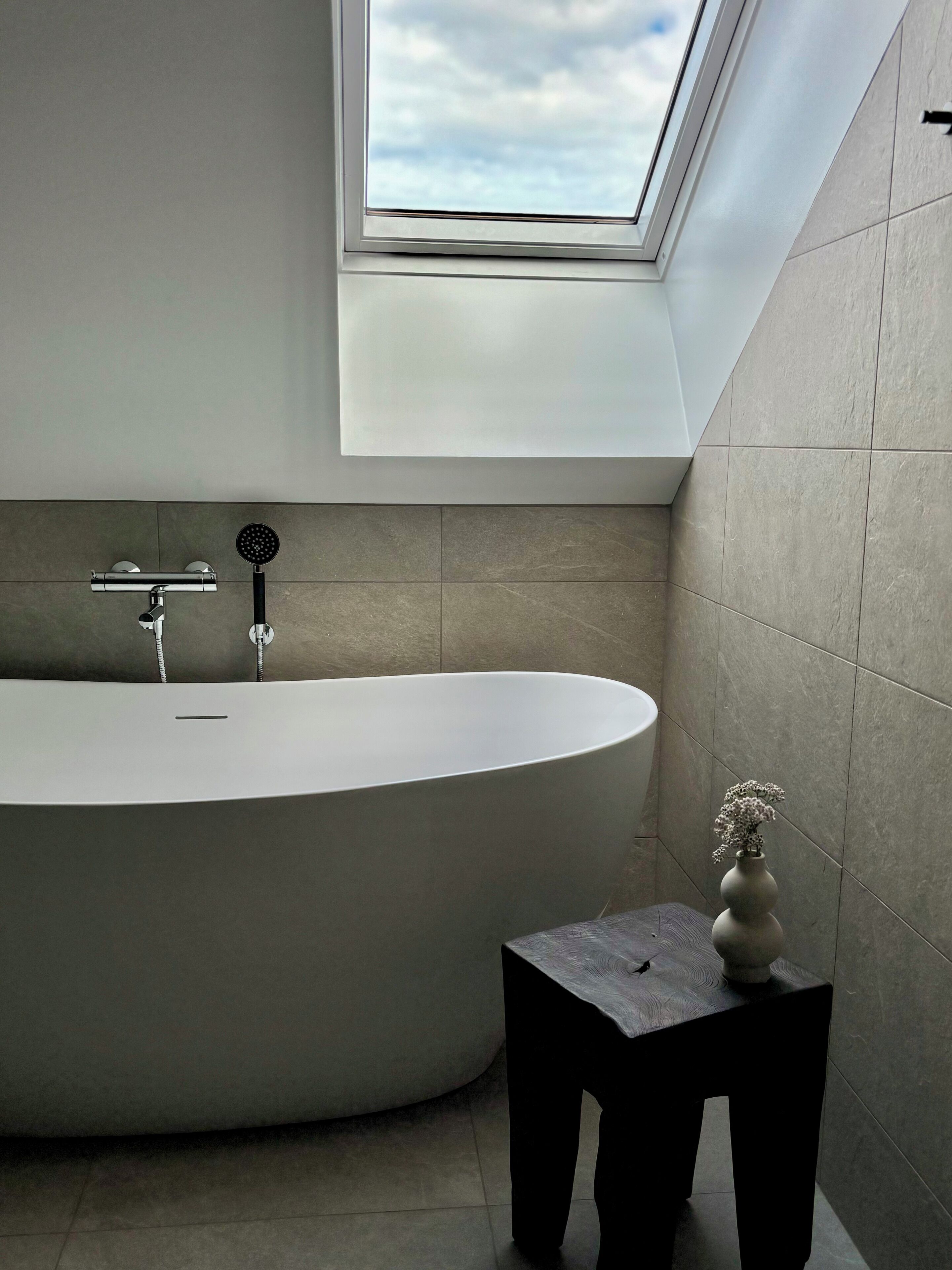 A modern bathroom with a freestanding bathtub, a skylight, and a small table with a vase.