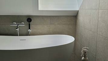 A modern bathroom with a freestanding bathtub, a skylight, and a small table with a vase.
