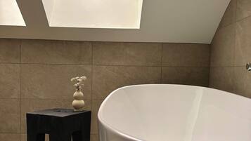 A modern bathroom with a skylight, a large bathtub, and a small stool with a vase.