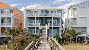 Un edificio residencial de varios pisos con balcones, una escalera central y un pasillo de madera que lleva a la entrada.