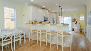 Una cocina con armarios blancos, una isla central con taburetes, un microondas y un refrigerador.