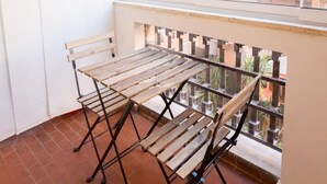 A balcony with a wooden table and chairs, a tiled floor, and a view of a brick building and greenery. - RoomApartment Rome: 1 Bedroom Apartment with Balcony  (Roma)