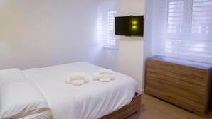A neatly made bed with white linens and a set of towels, a wooden nightstand, and a wall-mounted TV. - RoomApartment Rome: 1 Bedroom Apartment with Balcony  (Roma)