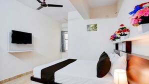 A hotel room with a bed, a TV mounted on the wall, a ceiling fan, and a window with curtains. - Shravanya Comforts (Bengaluru)