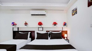 A hotel room with two beds, a ceiling fan, an air conditioning unit, and a wall-mounted shelf with flowers. - Shravanya Comforts (Bengaluru)