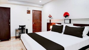 A hotel room with a large bed, a desk, a chair, and a wardrobe. - Shravanya Comforts (Bengaluru)