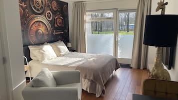 A bedroom with a large bed, a chair, a giraffe decoration, and a view of the outdoors through a sliding door.