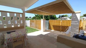 A covered patio area with a table and chairs, a wooden fence, and a view of a house in the background. - Cozy little house in Otranto, in the beautiful Baia dei Turchi. Pet Friendly. (Puglia)