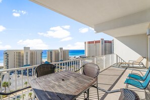 Un balcón con una mesa y sillas, con vista a una playa y edificios altos.