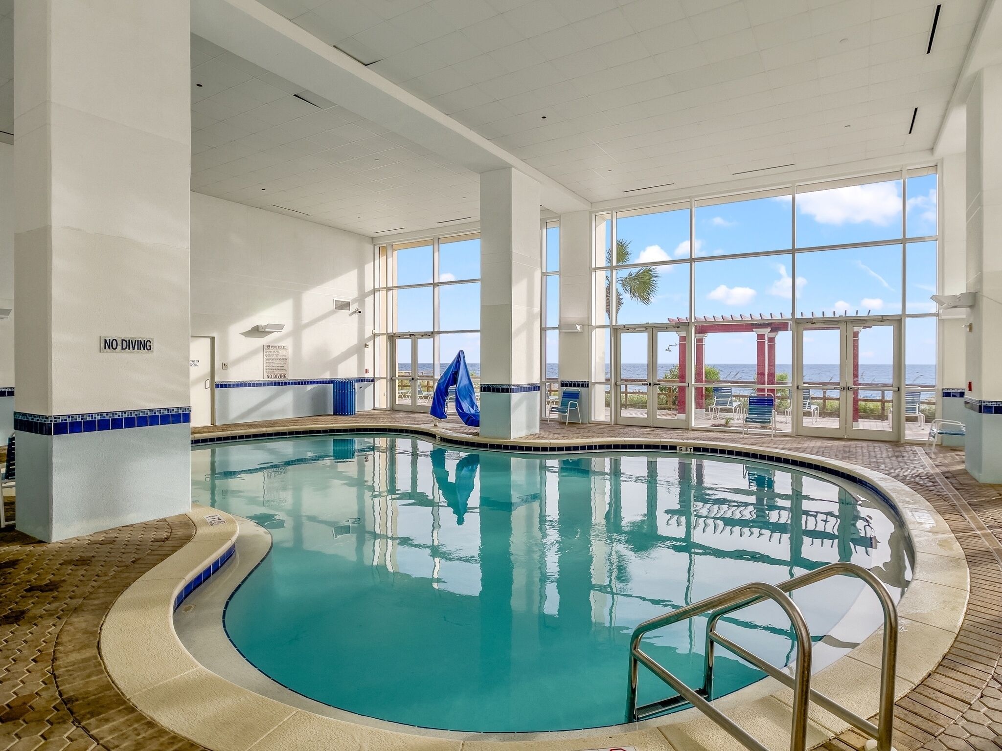 An indoor swimming pool with a view of the ocean through large windows.