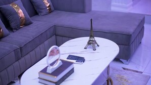 A modern living room with a grey sectional sofa, a white marble coffee table, a small Eiffel Tower model, a book, and a remote control. - PrimeAxis Apartment (Ilorin)