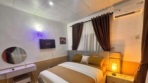 A hotel room with a bed, a desk, a TV, and an air conditioning unit. - PrimeAxis Apartment (Ilorin)