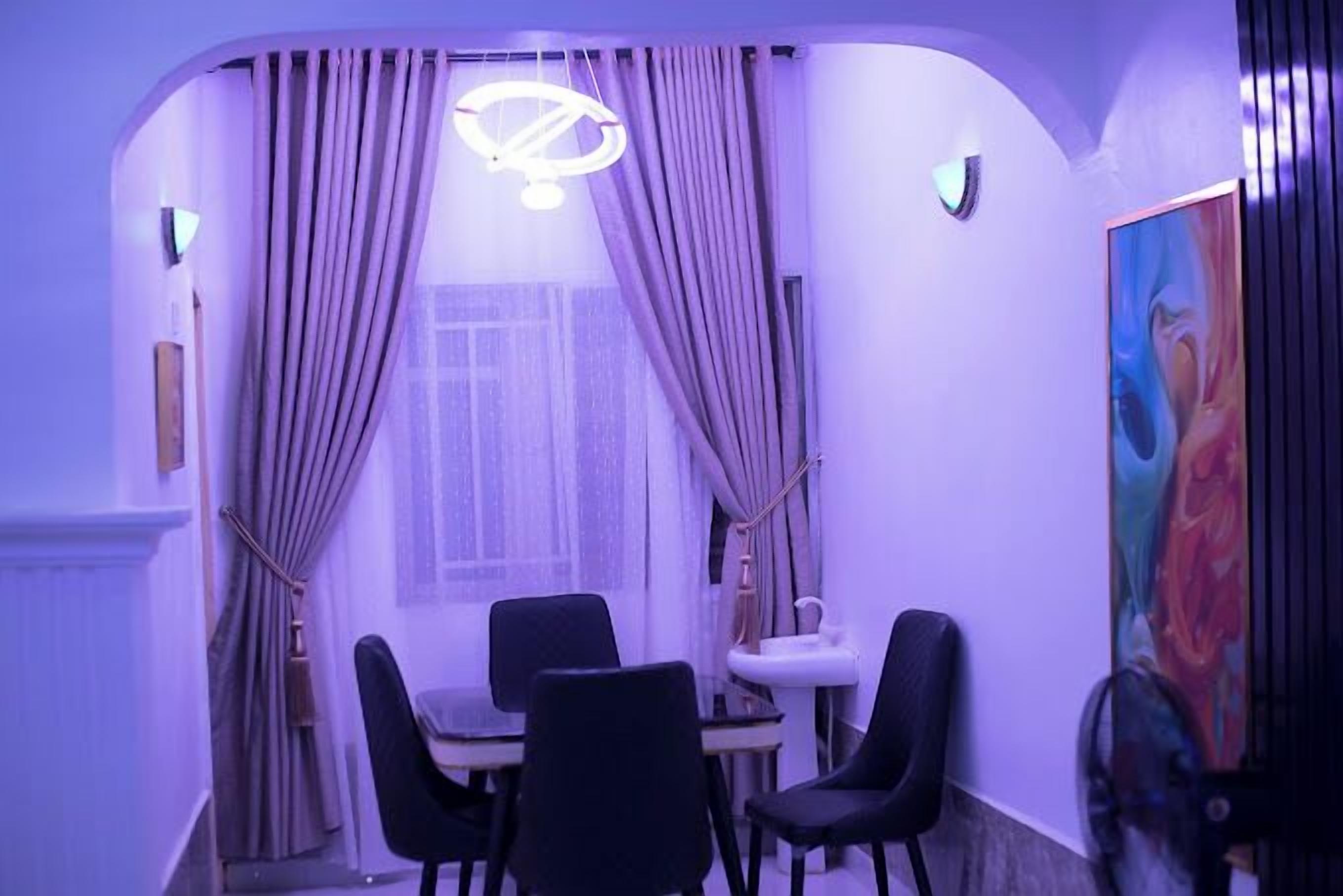 A dining area with a table and chairs, a pendant light, and a painting on the wall.