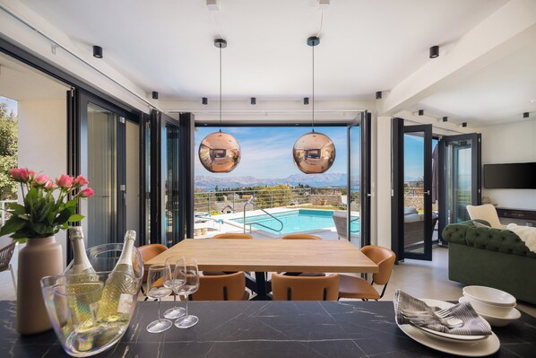 A modern dining area with a pool view, a table set for two, and a sofa in the background.