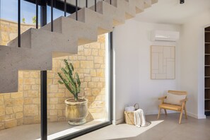 A modern interior with a staircase, a cactus plant, a chair, and a wall-mounted air conditioner.