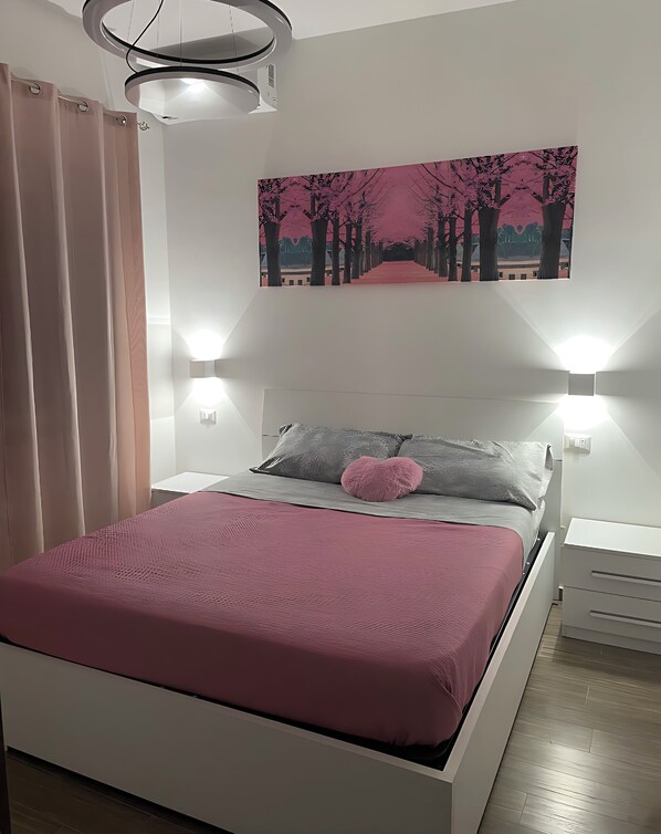 A modern bedroom with a bed, a painting, and two wall-mounted lights.