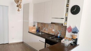 Een kleine keuken met witte kastjes, een gasfornuis, een spoelbak en een klok aan de muur.