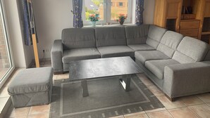 A modern living room with a grey sectional sofa, a small coffee table, and a window with curtains. - Vacation apartment 5 minutes from the sea, with dog. (Schönberg)