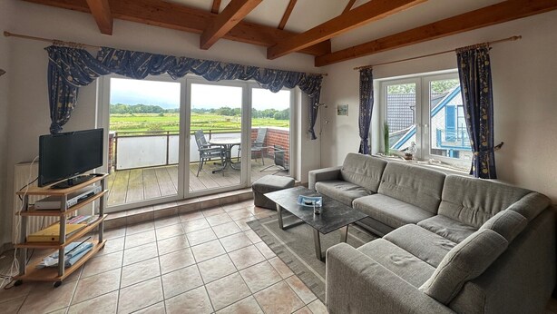 A living room with a sofa, a coffee table, a TV on a stand, and a balcony with a view of the countryside. - Vacation apartment 5 minutes from the sea, with dog. (Schönberg)