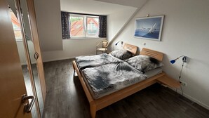 A bedroom with a bed, a chair, a window, and a painting on the wall. - Vacation apartment 5 minutes from the sea, with dog. (Schönberg)