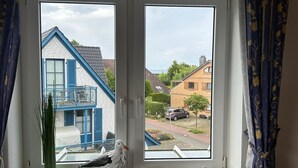 A window with a view of a residential area, a white bird on a stand, and a rope decoration. - Vacation apartment 5 minutes from the sea, with dog. (Schönberg)