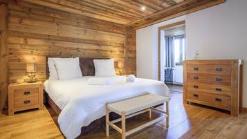 Une chambre aux murs lambrissés, avec un lit, des tables de chevet, un banc et une commode en bois.