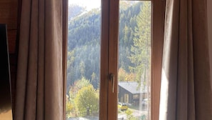 A room with a large window featuring wooden frames and beige curtains. - Hôtel des Muverans (Leytron)