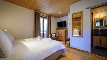 Une chambre à coucher avec un grand lit, un plafond en bois, une télévision, une commode en bois et une salle de bain avec un miroir.