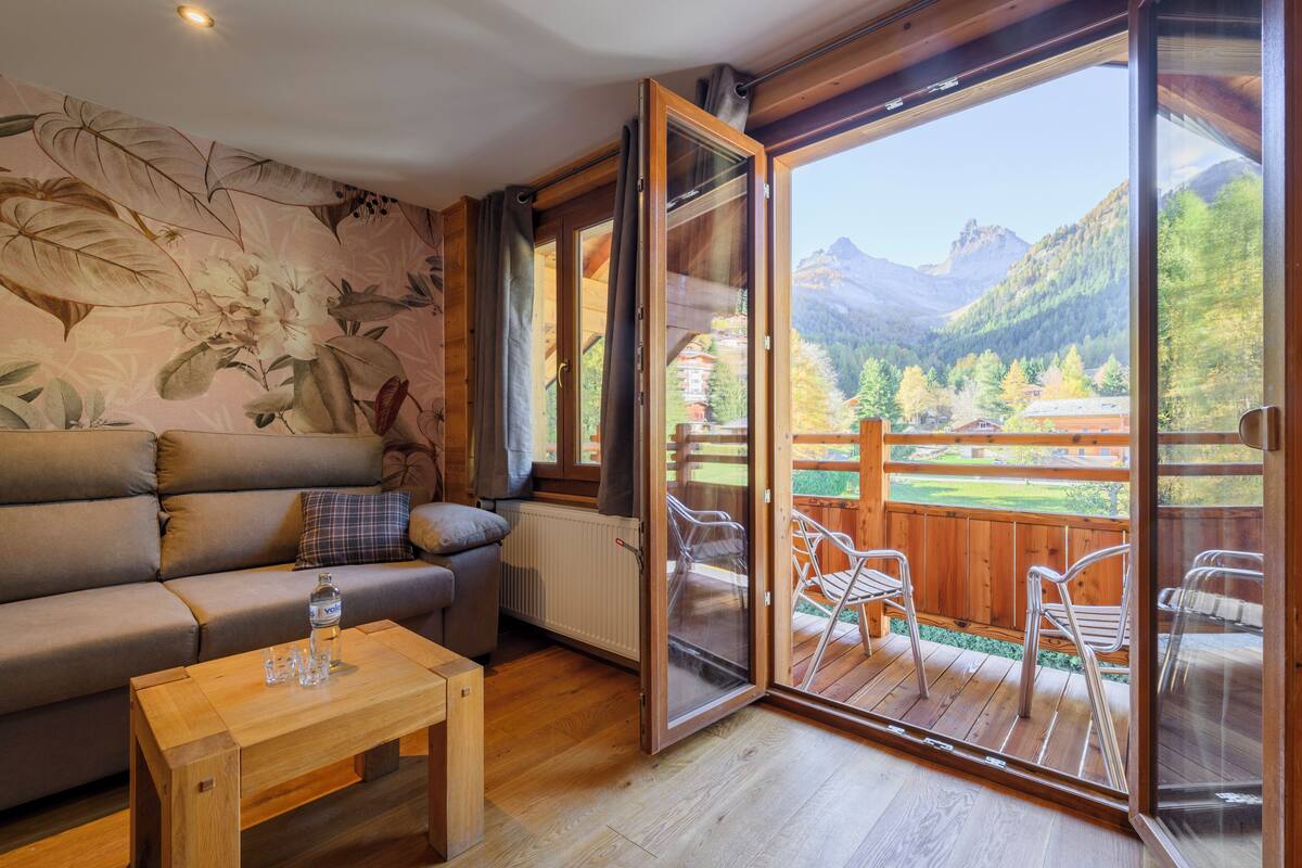 A cozy room with a sofa, a wooden table, and a sliding glass door leading to an outdoor deck with chairs.