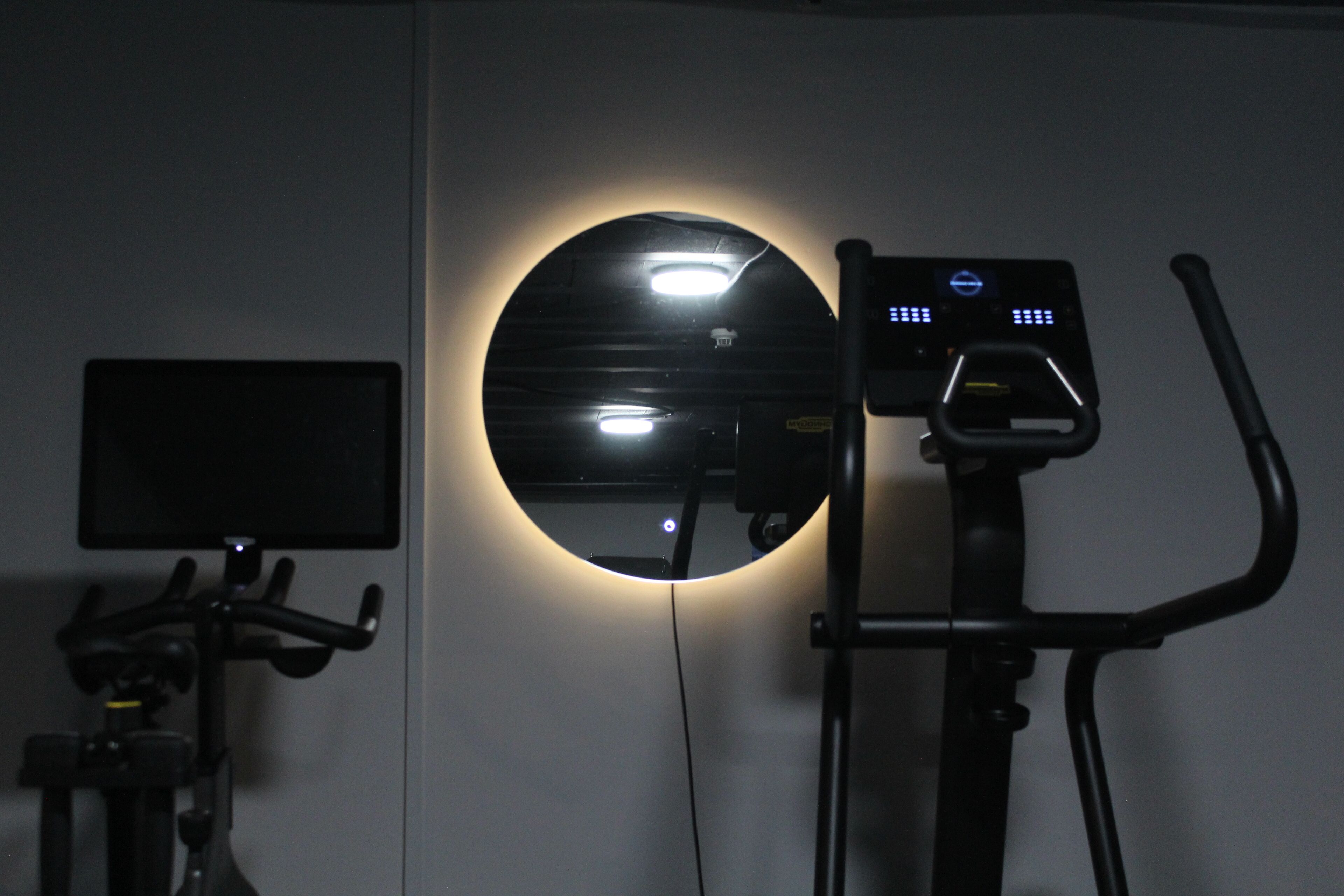 En stillastående motionscykel med digitalt display og et spejl på væggen.