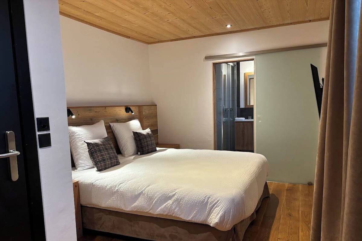 A bedroom with a large bed, wooden headboard, and a door leading to a bathroom.