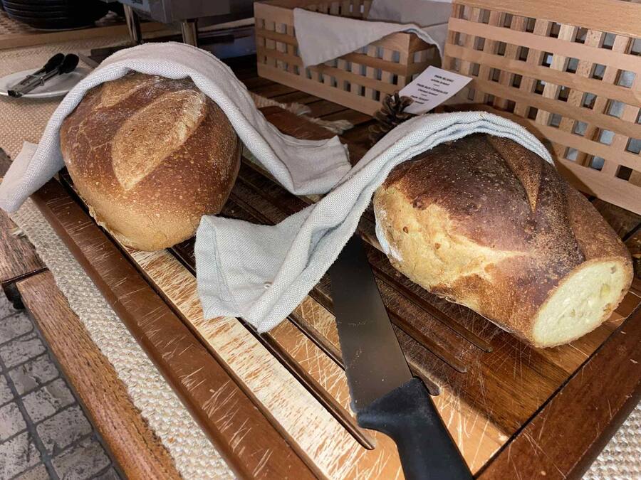 Two loaves of bread on a wooden cutting board, partially covered with cloths.