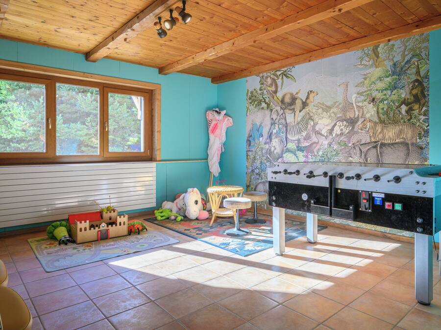 A room with a wooden ceiling, a large window, a mural of animals, a foosball table, and a play area with toys.