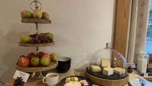 A breakfast setup with a fruit display, cheese, coffee, and a plate with toast and butter. - Hôtel des Muverans (Leytron)