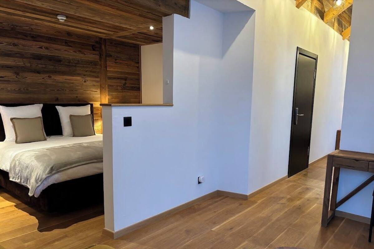 A bedroom with a bed, a wooden ceiling, a white wall, and a door.
