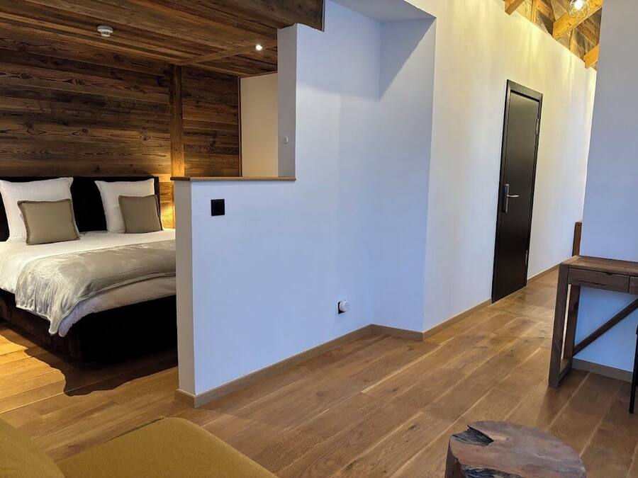A bedroom with a bed, a wooden ceiling, a white wall, and a door.