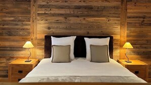 A wooden-paneled bedroom with a bed, two bedside lamps, and a nightstand. - Hôtel des Muverans (Leytron)