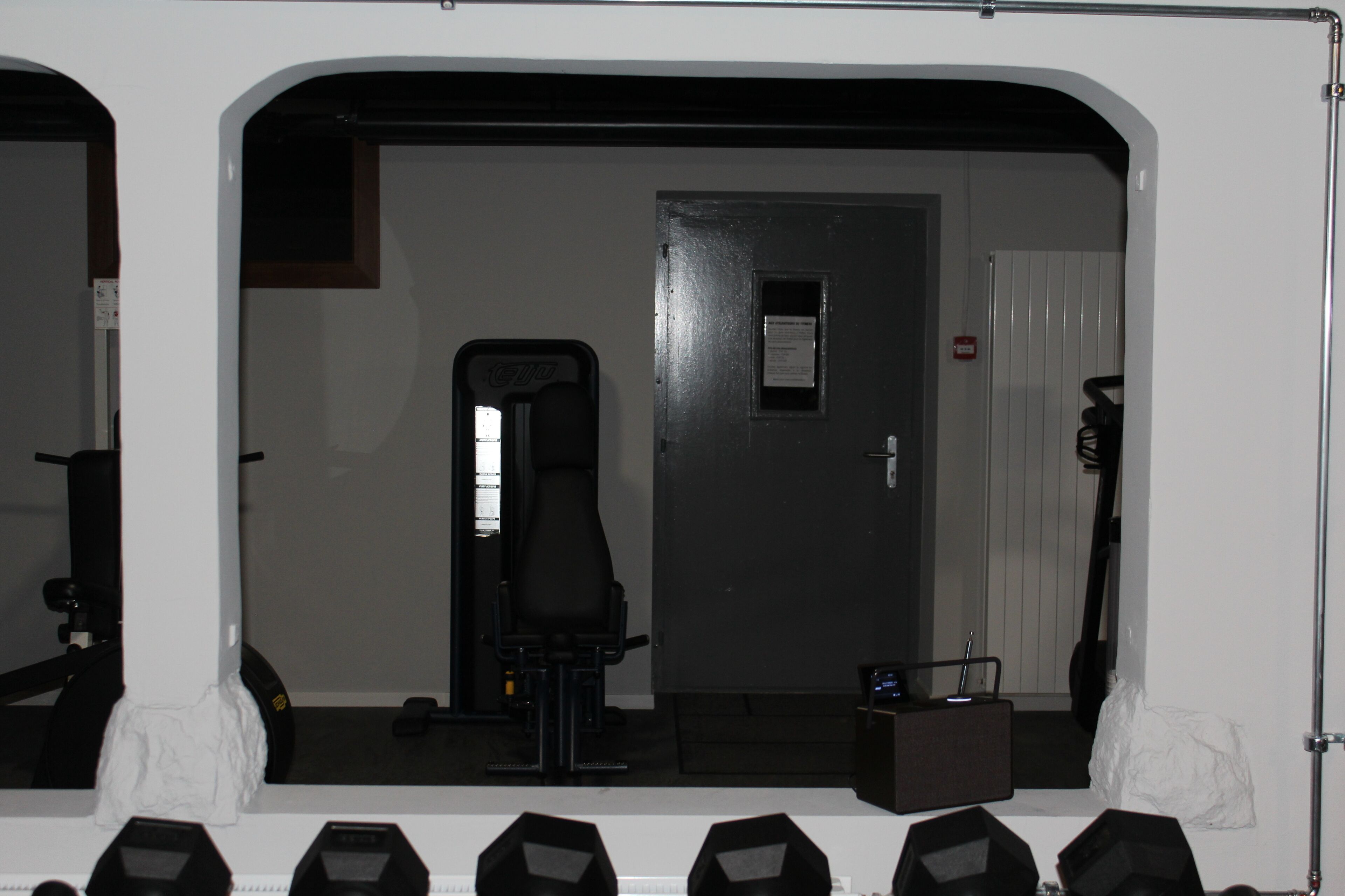 Une salle de sport équipée de matériel d’exercice, avec une porte et un mur blanc.