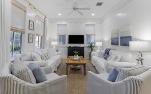 A spacious living room with two white sofas, a wooden coffee table, and a flat-screen TV.