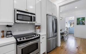 A modern kitchen with stainless steel appliances, white cabinetry, and a wooden floor.
