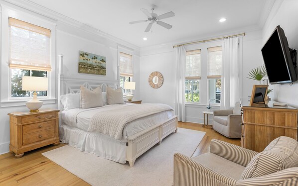 A bedroom with a large bed, bedside tables, a chair, a desk, and a television.