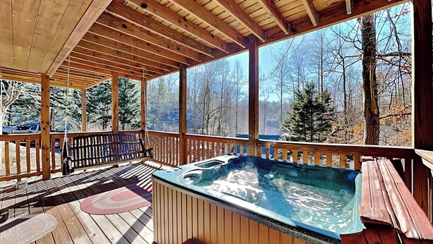 A wooden deck with a hot tub, wooden benches, and a view of the forest.